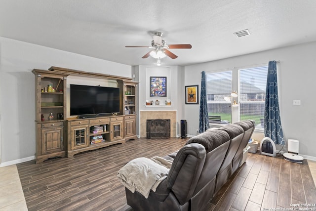 living room with dark wood-type flooring, a tile fireplace, ceiling fan, and a textured ceiling