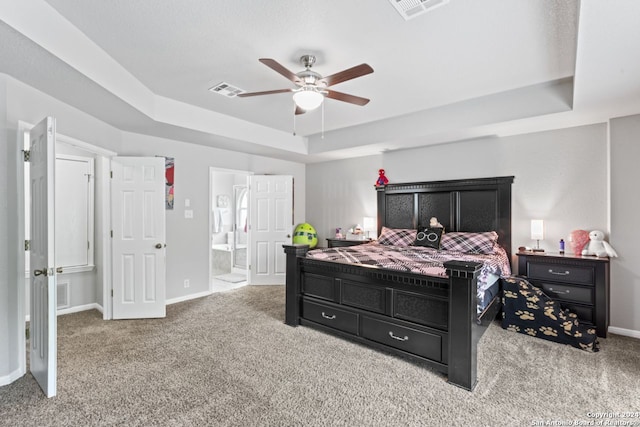 bedroom with ceiling fan, a raised ceiling, ensuite bath, and light colored carpet