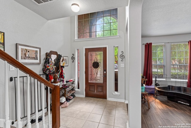 entrance foyer with a high ceiling, light tile floors, a textured ceiling, and a wealth of natural light