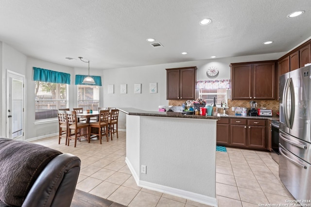 kitchen featuring dark stone counters, stainless steel refrigerator, tasteful backsplash, pendant lighting, and light tile flooring