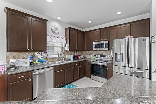 kitchen featuring stainless steel appliances, backsplash, dark brown cabinetry, dark stone countertops, and sink