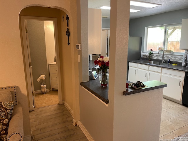 kitchen with black dishwasher, white cabinetry, light tile floors, and sink