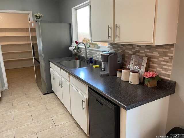 kitchen featuring backsplash, light tile floors, dishwasher, sink, and white cabinetry