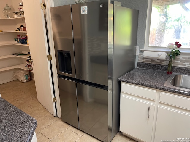 kitchen featuring light tile flooring, stainless steel refrigerator with ice dispenser, white cabinets, and sink