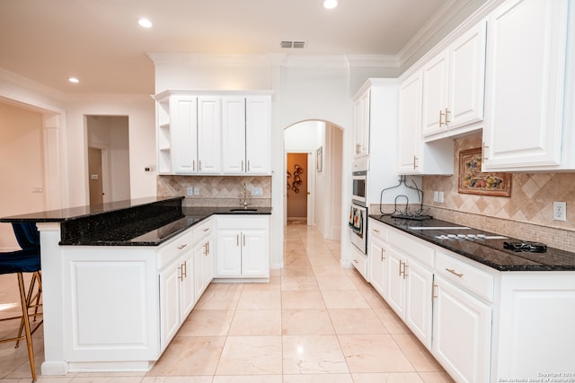 kitchen featuring crown molding, dark stone countertops, backsplash, a kitchen bar, and white cabinetry