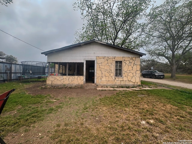 back of house with a trampoline, stone siding, and a lawn