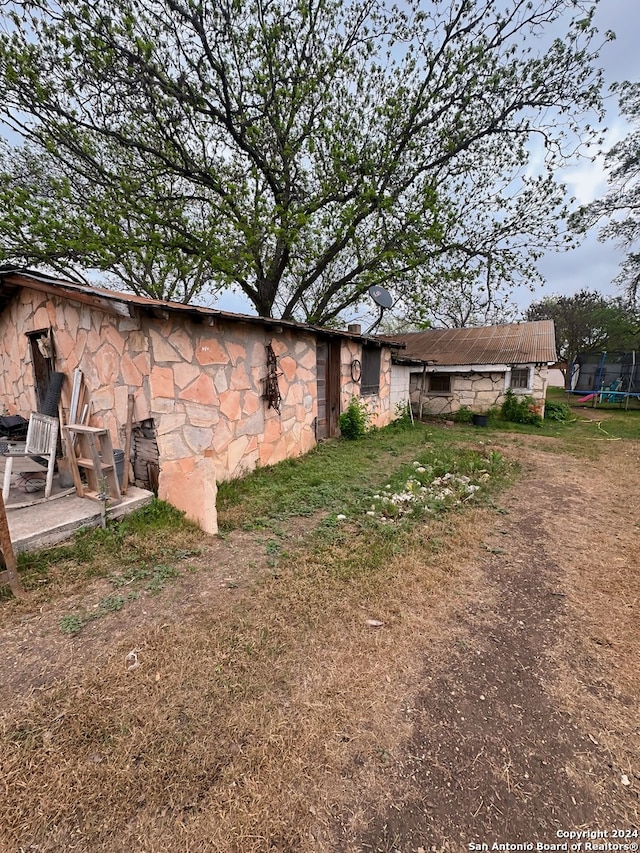 back of house with stone siding and a trampoline