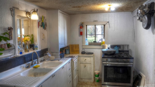 kitchen featuring a textured wall, gas range, light countertops, a textured ceiling, and a sink