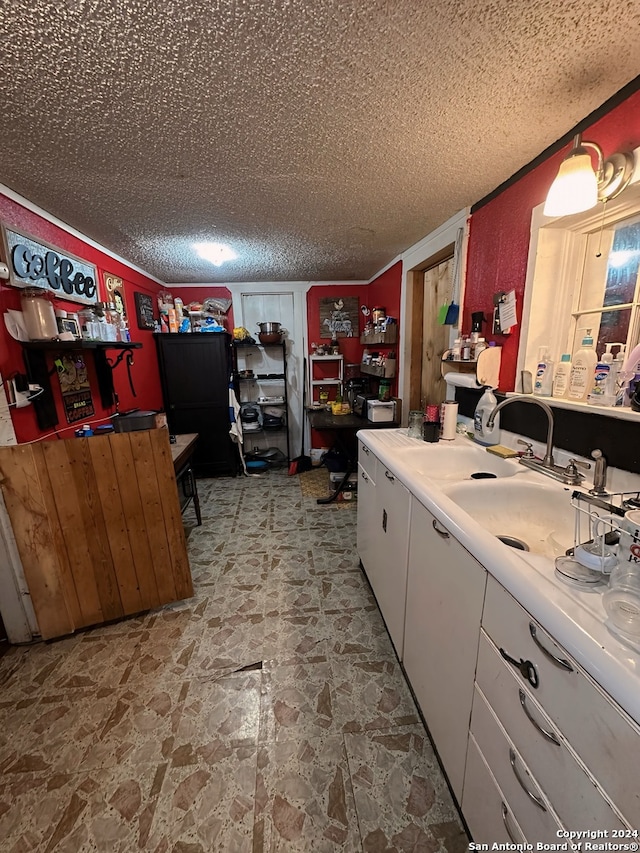 kitchen featuring a sink, a textured ceiling, white cabinets, and light countertops