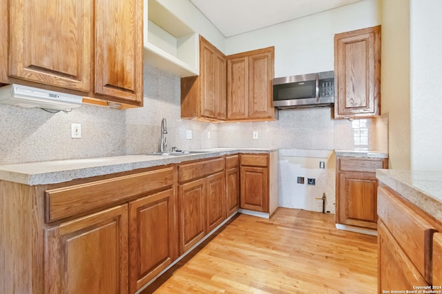 kitchen with backsplash, fume extractor, sink, and light wood-type flooring