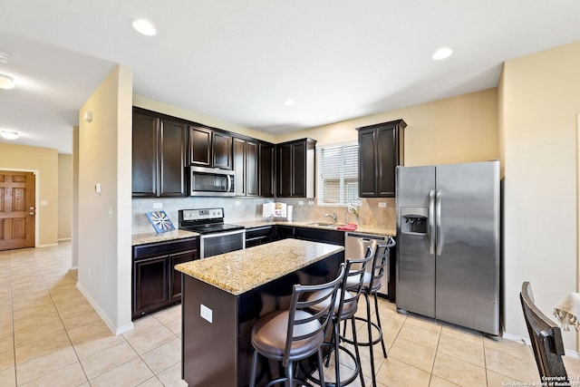 kitchen featuring stainless steel appliances, a center island, a kitchen breakfast bar, light tile flooring, and backsplash