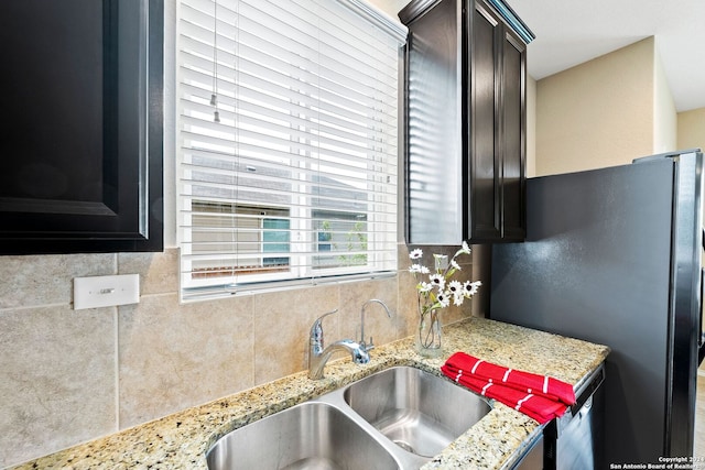 kitchen with light stone countertops, stainless steel refrigerator, dark brown cabinetry, and sink