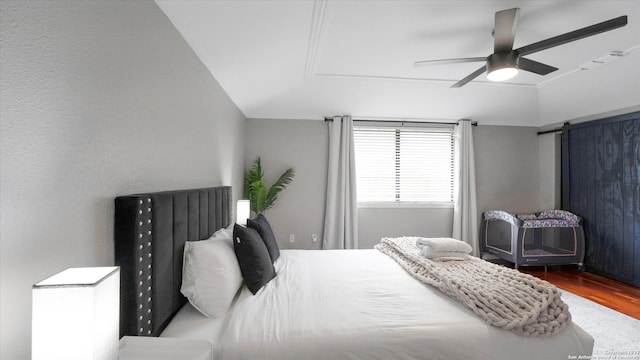 bedroom featuring a barn door, ceiling fan, and hardwood / wood-style flooring