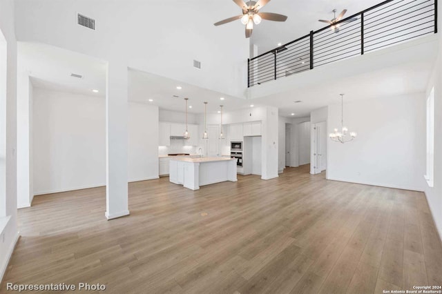 unfurnished living room with ceiling fan with notable chandelier, sink, a towering ceiling, and light hardwood / wood-style floors