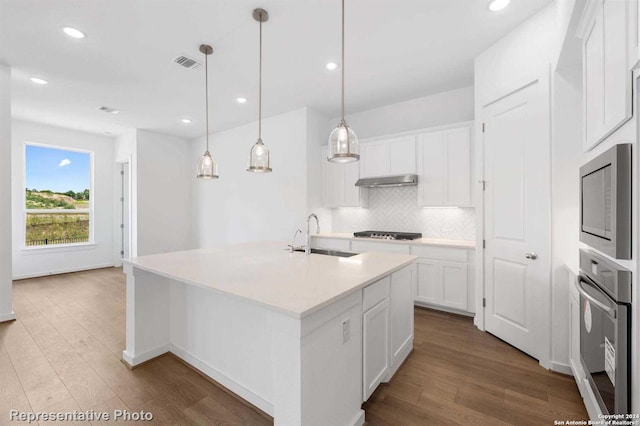 kitchen featuring appliances with stainless steel finishes, sink, tasteful backsplash, light wood-type flooring, and an island with sink