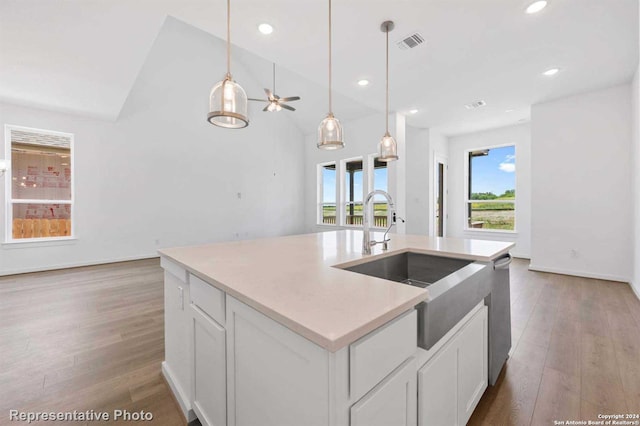 kitchen featuring pendant lighting, wood-type flooring, white cabinetry, stainless steel dishwasher, and an island with sink