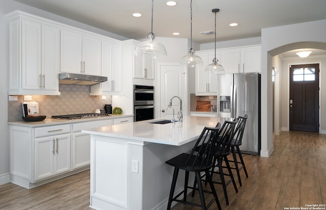 kitchen featuring pendant lighting, backsplash, a center island with sink, stainless steel appliances, and dark wood-type flooring