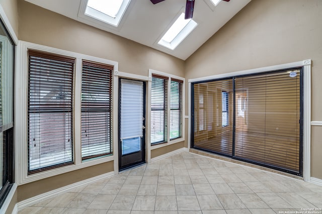 unfurnished room with a skylight, ceiling fan, light tile floors, and high vaulted ceiling