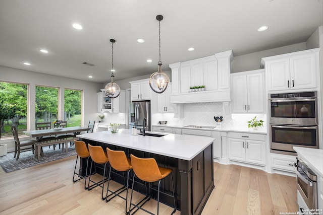 kitchen with backsplash, an island with sink, light hardwood / wood-style flooring, stainless steel appliances, and pendant lighting