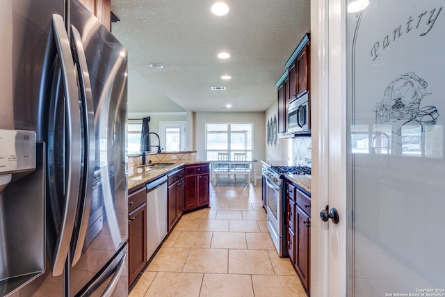 kitchen featuring light stone counters, light tile floors, stainless steel appliances, a textured ceiling, and sink