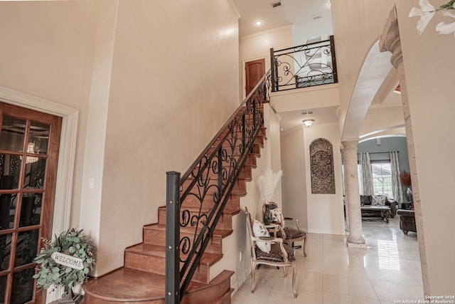 staircase featuring a towering ceiling, ornamental molding, light tile floors, and ornate columns