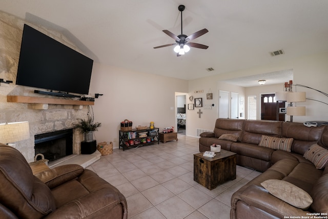 living room featuring ceiling fan, a stone fireplace, and light tile patterned flooring