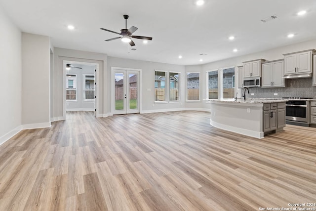 kitchen with gray cabinetry, a kitchen island with sink, light wood-type flooring, appliances with stainless steel finishes, and tasteful backsplash