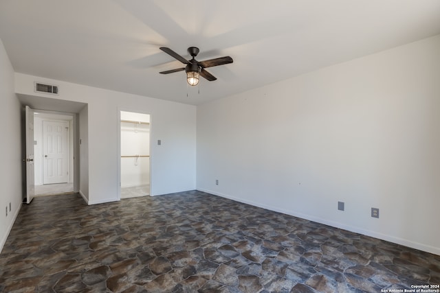 unfurnished bedroom featuring ceiling fan, dark tile flooring, and a spacious closet