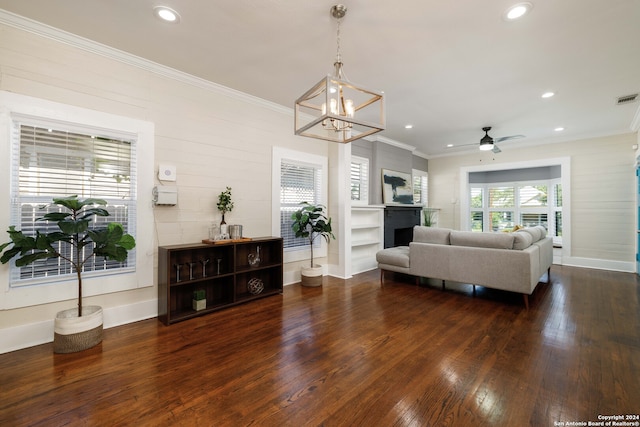 living room with crown molding, dark wood-type flooring, and ceiling fan with notable chandelier