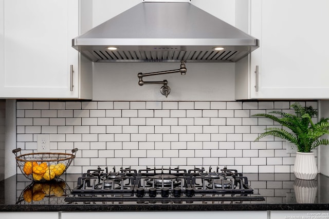 kitchen featuring dark stone counters, tasteful backsplash, white cabinets, wall chimney range hood, and black gas stovetop