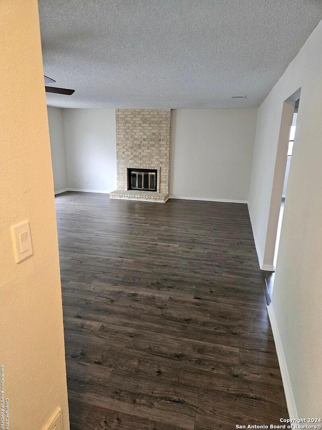 unfurnished living room featuring brick wall, a fireplace, dark hardwood / wood-style floors, and a textured ceiling