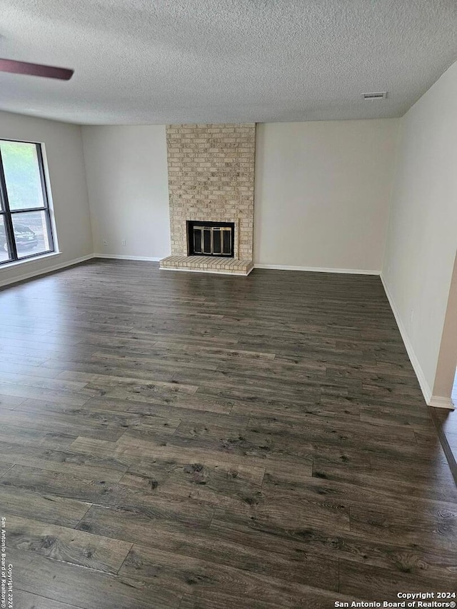 unfurnished living room featuring brick wall, a textured ceiling, dark hardwood / wood-style flooring, and a fireplace