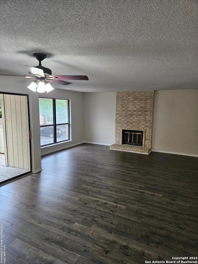 unfurnished living room featuring ceiling fan, a fireplace, brick wall, a textured ceiling, and dark hardwood / wood-style flooring