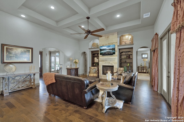 living room featuring coffered ceiling, ceiling fan, dark wood-type flooring, beam ceiling, and a stone fireplace