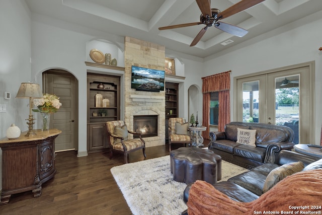 living room with ceiling fan, beamed ceiling, coffered ceiling, dark wood-type flooring, and a stone fireplace