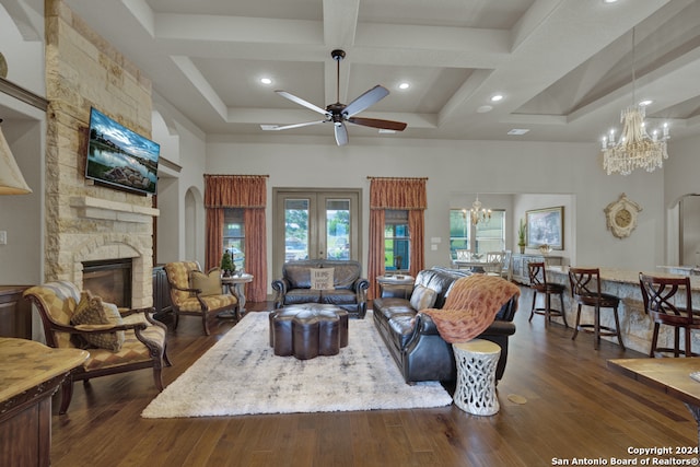 living room with coffered ceiling, ceiling fan with notable chandelier, dark wood-type flooring, a towering ceiling, and a stone fireplace