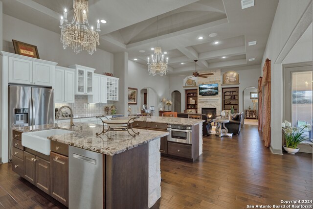 kitchen featuring a center island with sink, coffered ceiling, tasteful backsplash, white cabinetry, and a stone fireplace