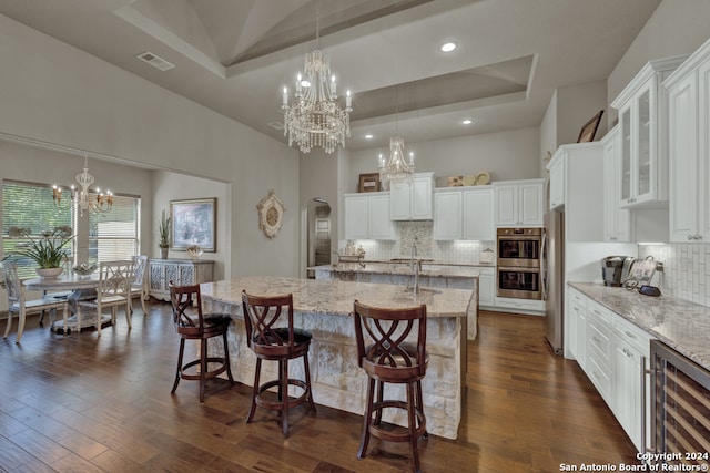 kitchen with a breakfast bar area, white cabinetry, backsplash, a raised ceiling, and a kitchen island with sink