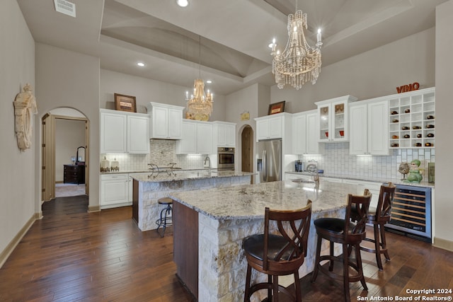 kitchen with an inviting chandelier, appliances with stainless steel finishes, a raised ceiling, and a center island with sink