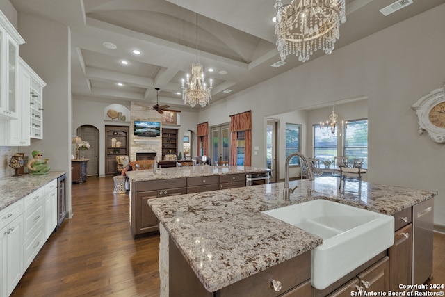 kitchen with a large fireplace, coffered ceiling, a kitchen island with sink, and white cabinetry