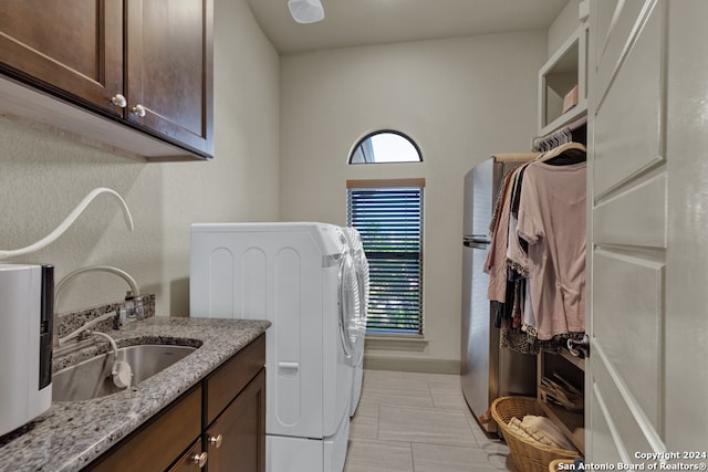 clothes washing area with washer and clothes dryer, sink, cabinets, and light tile flooring