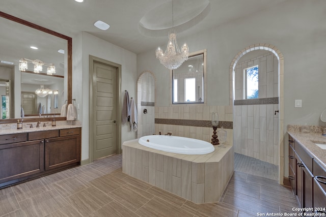 bathroom featuring tile flooring, a relaxing tiled bath, a chandelier, and vanity with extensive cabinet space