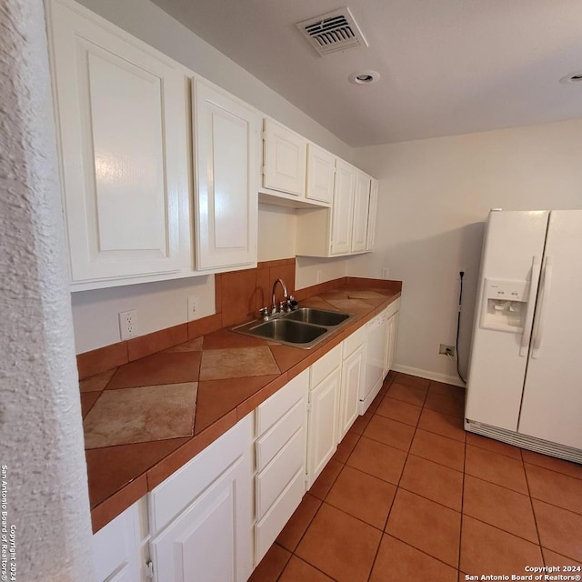 kitchen with dark tile floors, white appliances, white cabinetry, and sink