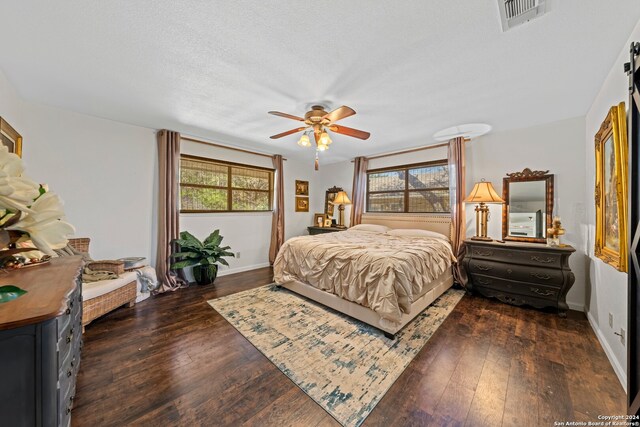 bedroom with a barn door, a textured ceiling, dark hardwood / wood-style floors, and ceiling fan