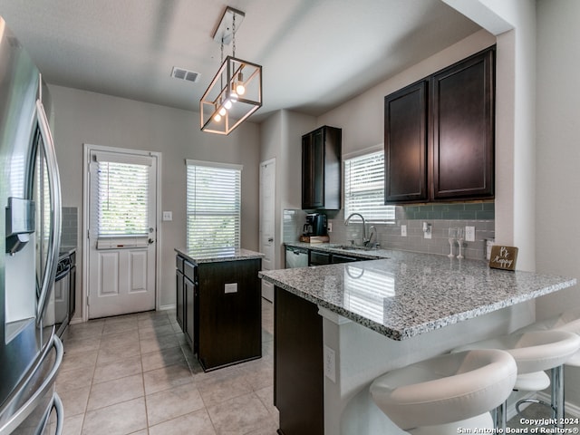 kitchen with light stone counters, stainless steel refrigerator, backsplash, kitchen peninsula, and pendant lighting