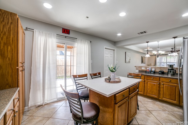 kitchen featuring light tile floors, a center island, a kitchen breakfast bar, a chandelier, and pendant lighting