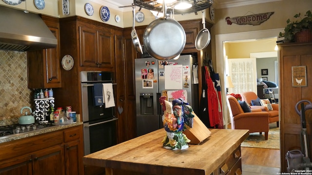 kitchen featuring backsplash, crown molding, stainless steel appliances, butcher block counters, and ventilation hood