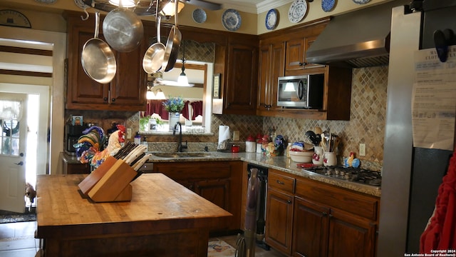 kitchen featuring appliances with stainless steel finishes, wood counters, backsplash, wall chimney range hood, and sink