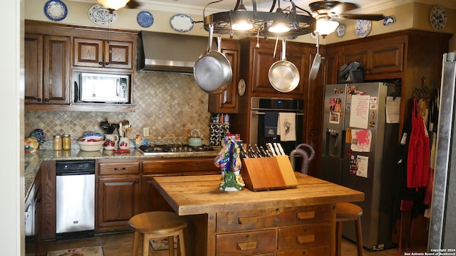 kitchen featuring wall chimney range hood, ceiling fan, stainless steel appliances, backsplash, and wooden counters