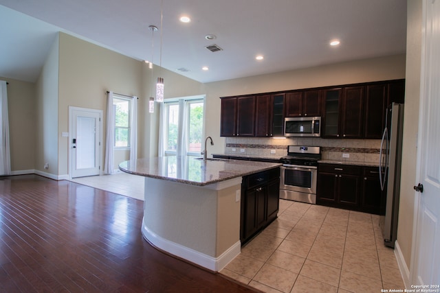 kitchen with an island with sink, decorative light fixtures, light hardwood / wood-style flooring, appliances with stainless steel finishes, and backsplash